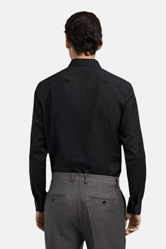 Chemise noire à manches longues de MANGO, vue de derrière, associée à un pantalon gris.