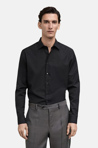 Chemise noire à manches longues de MANGO, portée avec un pantalon gris.