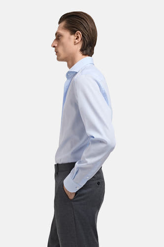 Chemise bleue à manches longues de MANGO, en profil, associée à un pantalon gris.