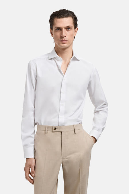 Wit overhemd met lange mouwen van MANGO, gedragen met beige pantalon en een hand in de zak.
