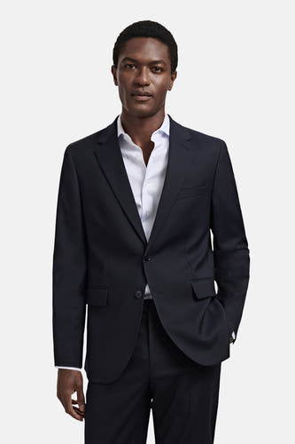Blauwe blazer van MANGO, met een lichtblauw gestreept overhemd eronder, en een hand in de zak.
