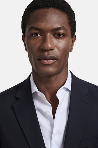 Blauwe blazer van MANGO, gedragen over een lichtblauw gestreept overhemd, in een close-up van een model.
