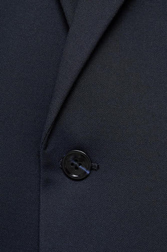 Blauwe blazer van MANGO, met een zwarte knoop en subtiele textuur.

