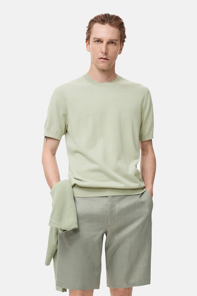 T-shirt vert avec manches courtes de MANGO, porté avec des shorts coordonnés et un gilet à la main.