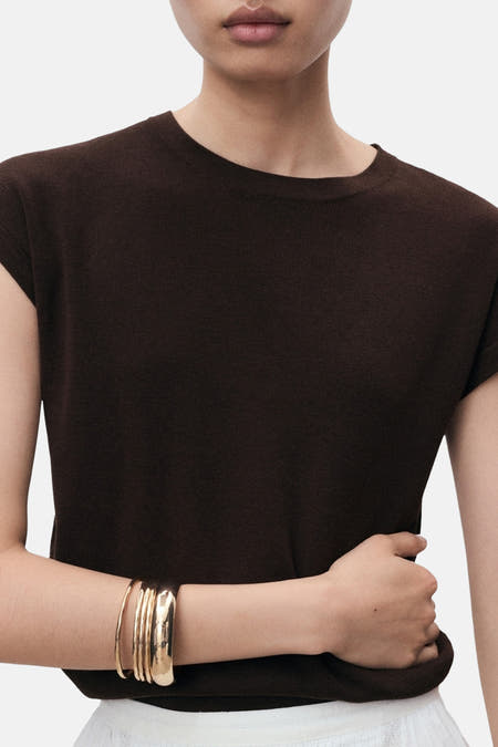 Bruine top zonder mouwen van MANGO, met een geribbelde textuur en gouden armbanden.
