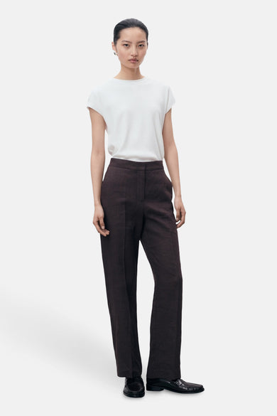 Een vrouw draagt een witte top en een bruine pantalon met zwarte schoenen.