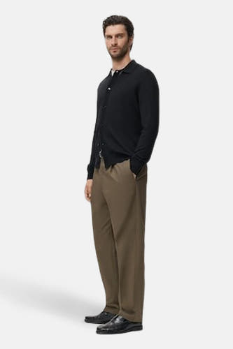 Gilet bleu de MANGO, porté par un modèle avec un cardigan noir et des pantalons marron.