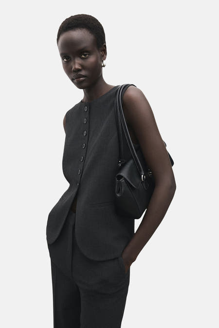 Grijs blazer van MANGO, gedragen door een model met een zwarte tas en bijpassende broek.

