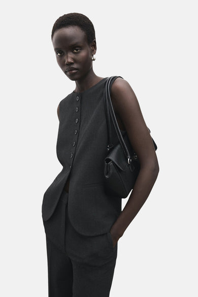Blazer gris de MANGO porté par un modèle avec un sac noir et une pantalon coordonné.
