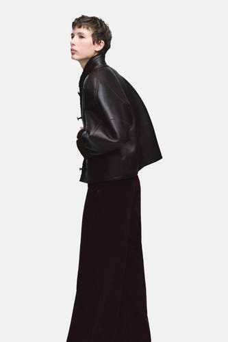 Veste marron de MANGO portée avec un pantalon bordeaux large, présenté latéralement contre un fond uni.