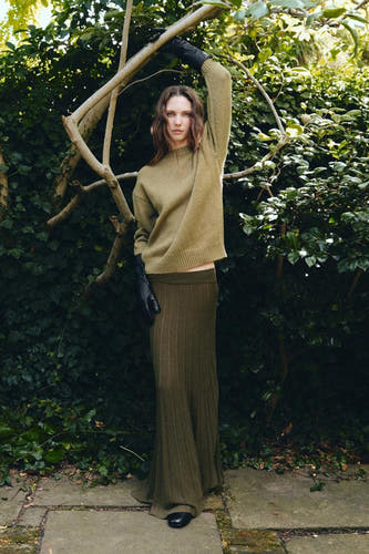 Lange kaki rok van MANGO, geribbelde textuur, gecombineerd met een groene trui en zwarte leren handschoenen.