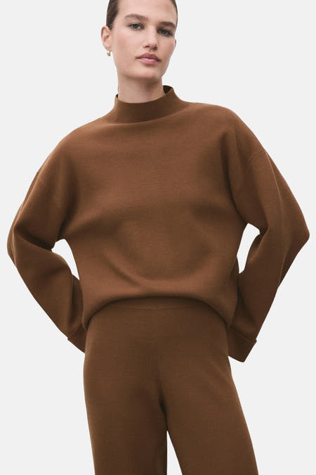 Pull marron avec col montant de MANGO, vu de derrière avec un pantalon coordonné et une queue de cheval.