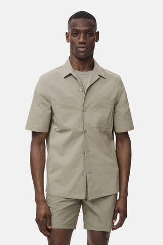 T-shirt kaki avec manches courtes de MANGO, avec poches po po et et col, porté avec un T-shirt gris et des shorts coordonnés.