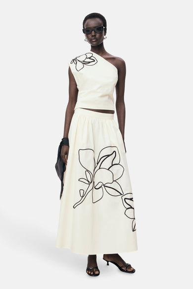 Ecru mouwloze blouse van MANGO, met zwarte bloemmotieven en gedragen met een bijpassende lange rok.
