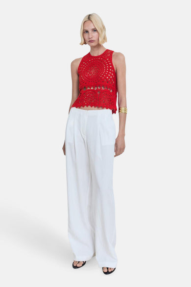 Mouwloze rode blouse van MANGO, met een gehaakt patroon, gedragen met witte pantalon en sandalen.