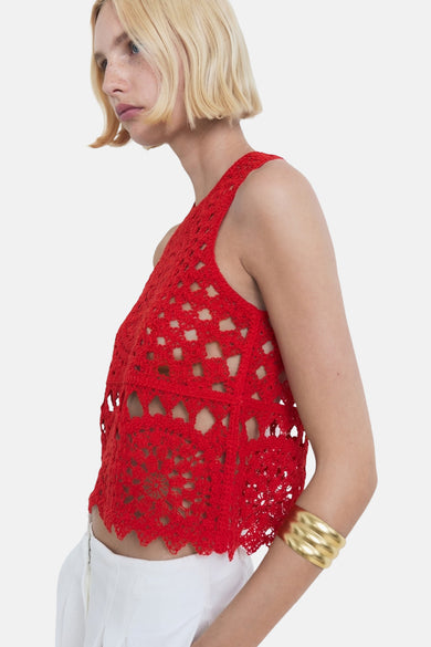 Rode mouwloze blouse van MANGO, met open haakpatroon en gedragen met een gouden armband.
