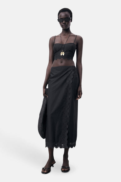 Zwarte lange rok van MANGO, met kanten details aan de zijkant en zoom, gecombineerd met een zwarte top en een ketting.

