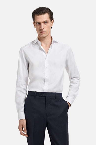 Wit overhemd met lange mouwen van MANGO, gedragen met een donkerblauwe pantalon en een hand in de zak.
