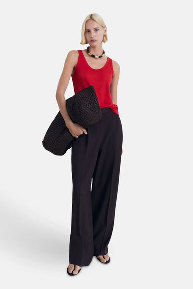 T-shirt rouge de MANGO, porté avec un pantalon noir et une grande valise marron foncé.