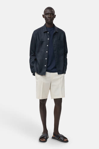 Chemise bleue marine à manches longues de MANGO, portée avec un T-shirt bleu et des short beige be sandales.