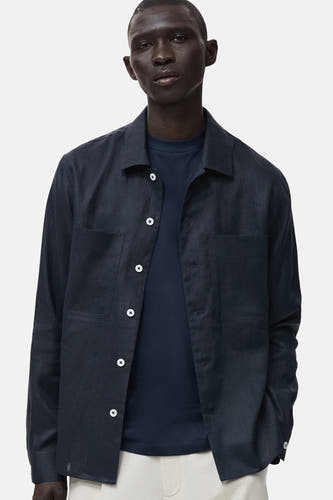 Chemise bleue marine à manches longues de MANGO, avec des boutons blancs et des poches brodées, portée sur un T-shirt bleu marine.