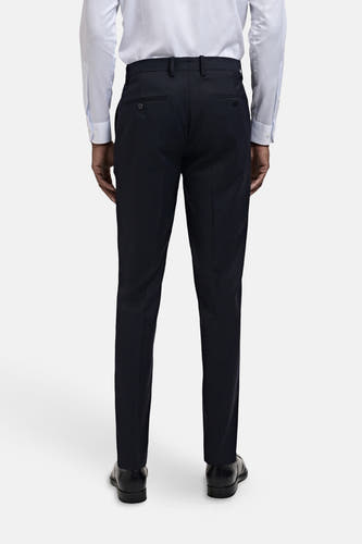 Pantalon de costume bleu MANGO, vu de l'arrière, avec des boutons sur les poches arrière et porté avec un chemisier bleu clair.