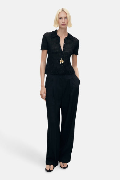 Pantalon noir de MANGO, avec des jambes larges et des poches, porté avec un haut noir et une chaîne d'or.