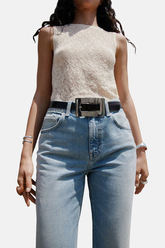 Lichtblauwe flared jeans van MANGO, met een zwarte riem met grote zilverkleurige gesp, gedragen met een kanten top.
