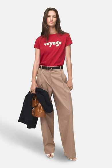 Rood T-shirt met korte mouwen van MANGO, met witte opdruk 'voyage', gecombineerd met een bruine broek en accessoires.
