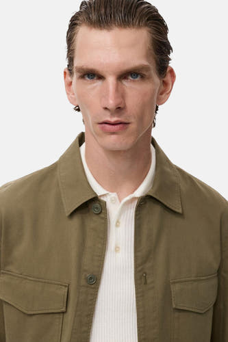 Groen hemd (lange mouwen) van MANGO, gedragen over een wit geribbeld poloshirt met kraag.