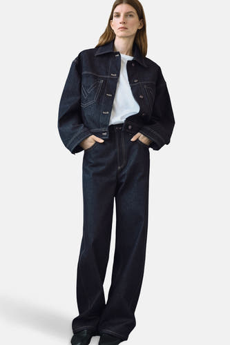 Donkerblauwe jeansjas van MANGO, met witte stiksels en gedragen over een wit t-shirt met donkere jeans.
