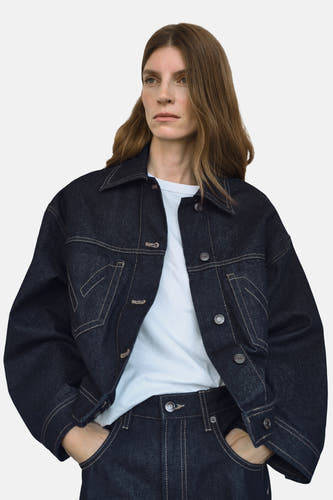 Donkerblauwe jeansjas van MANGO met contrasterende stiksels en knoopsluiting, gedragen over een wit T-shirt en jeans.
