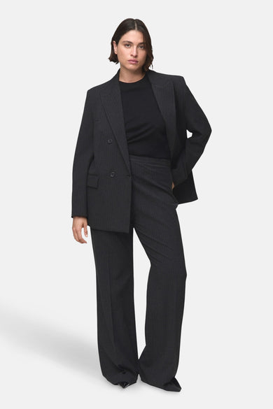 Grijze kostuumbroek van MANGO, met krijtstreep en wijde pijpen, gecombineerd met een zwart shirt en blazer.
