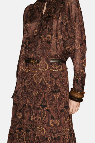 Bruine blouse met lange mouwen van MANGO, met een paisley-patroon, een zwarte riem en bruine armbanden.
