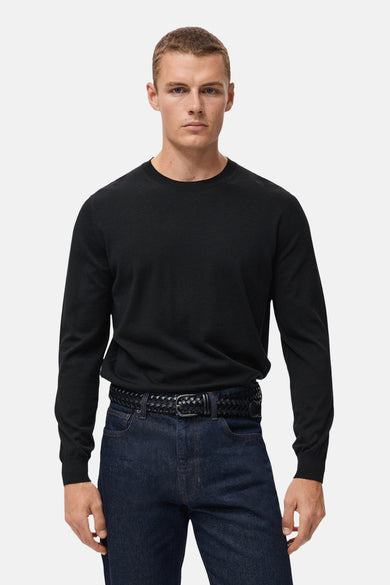 Sweat-shirt noir à col rond de MANGO, porté avec une ceinture tressée et des jeans foncés.