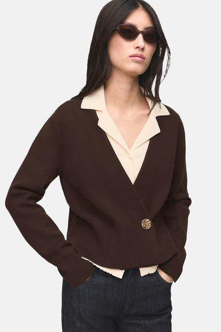 Bruin gilet van MANGO met een enkele gouden knoop, gedragen over een lichtgekleurde blouse en donkere jeans.
