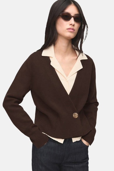 Bruin gilet van MANGO met een enkele gouden knoop, gedragen over een lichtgekleurde blouse en donkere jeans.

