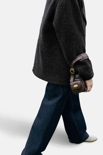 Jean denim bleu marine spécial fit de MANGO, avec une coupe décontractée et porté avec un blouson gris et une sacoche en cuir.