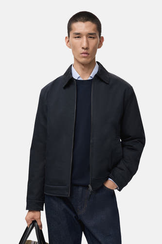 Blauwe, korte jas van MANGO, gedragen over een donkerblauwe trui en een lichtblauw overhemd, met donkere jeans.
