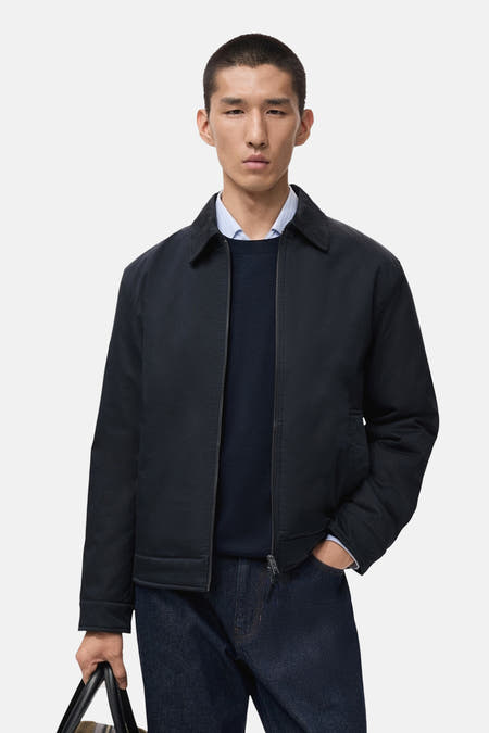 Manteau bleu court de MANGO porté sur une chemise bleue foncée et un blazer bleu clair, avec des jeans noirs.
