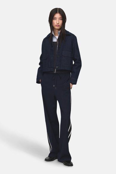 Pantalon bleu de MANGO avec des rayures blanches sur les côtés, porté avec un gilet bleu marine et des chaussures noires.