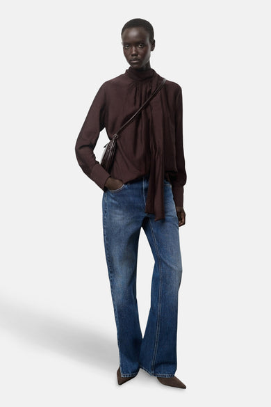 Bruine blouse met lange mouwen van MANGO, met een hoge kraag en gedrapeerde details, gecombineerd met een blauwe jeans.

