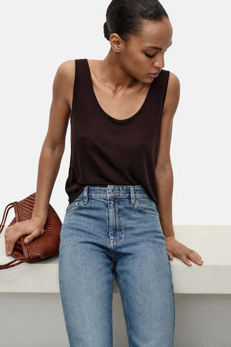 Middenblauwe mom jeans van MANGO, gecombineerd met een bruin hemdje en een geweven tas.