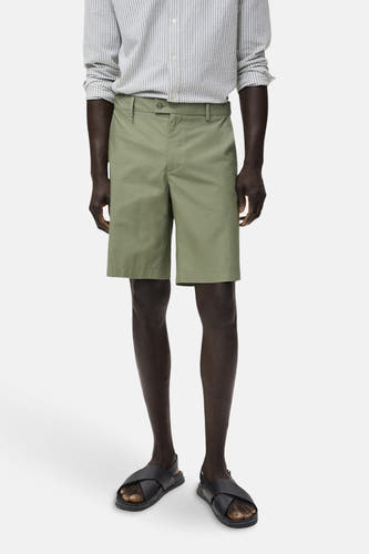 Groene short van MANGO, gecombineerd met een gestreept overhemd en zwarte sandalen.
