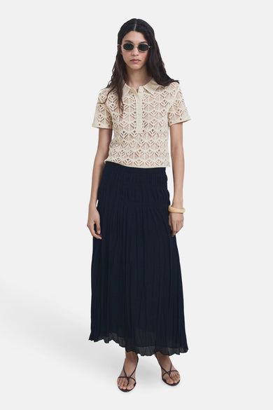 Beige trui met ronde hals van MANGO, met ajourpatroon en korte mouwen, gecombineerd met een lange, donkere rok en sandalen.
