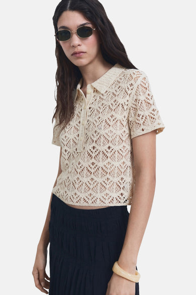 Beige trui met ronde hals van MANGO, met open ajour breisel, gedragen met een donkere rok en een opvallende armband.
