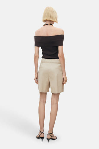 Beige bermuda van MANGO, met een hoge taille en achterzakken, gedragen met een zwarte top en hakken.
