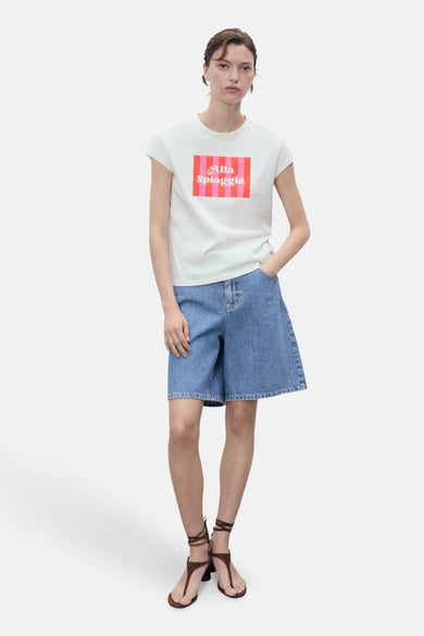 Wit T-shirt met korte mouwen van MANGO, met roze 'Alla Spiaggia' tekst op de borst, gecombineerd met denim bermuda en sandalen.