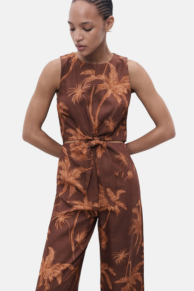 Bruine jumpsuit van MANGO met palmboomprint en een knoopdetail aan de voorkant.