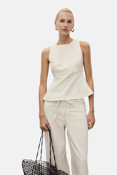 Mouwloze blouse in ecru van MANGO, met een peplum silhouet, gecombineerd met een broek en een nettas.
